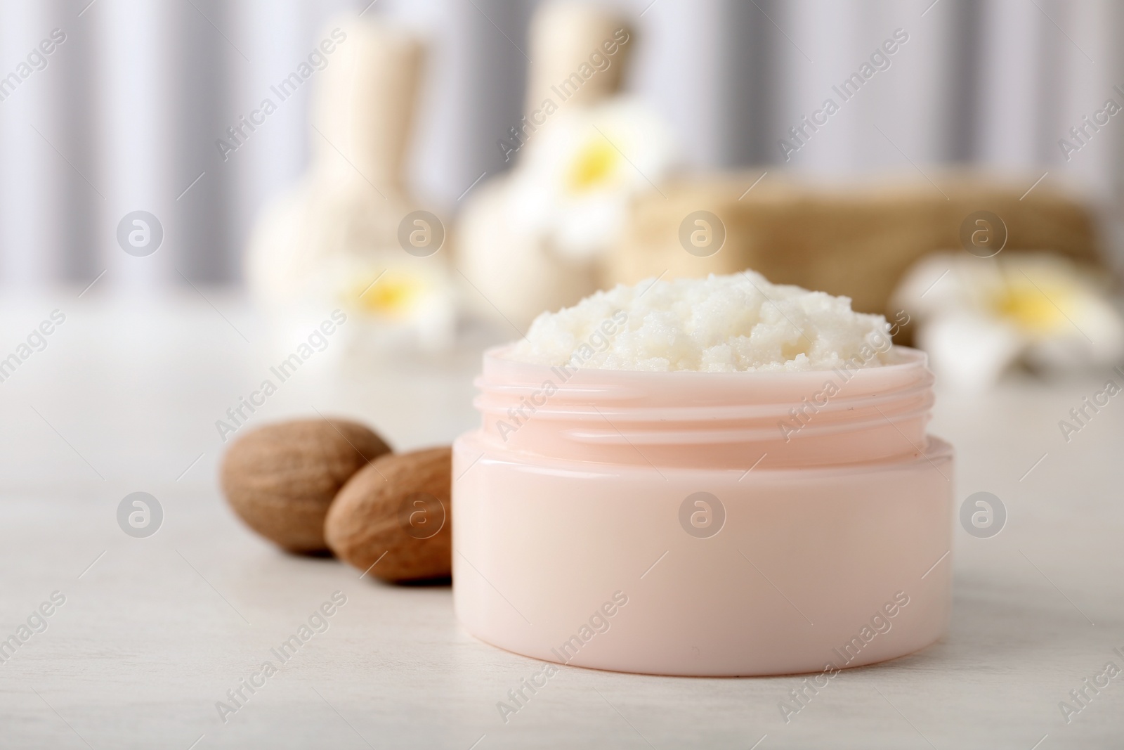 Photo of Jar of shea butter and nuts on table against blurred background. Space for text