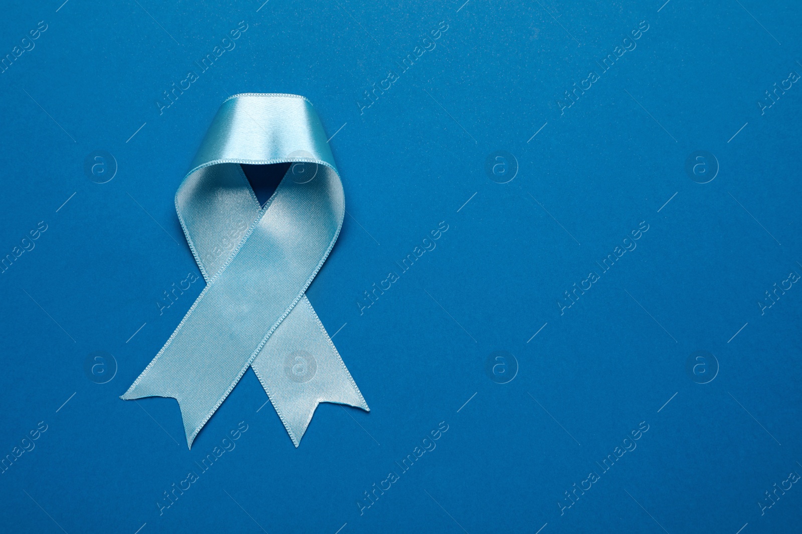 Photo of Light blue awareness ribbon on color background, top view. Space for text