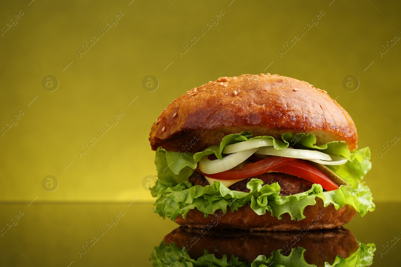 Photo of Delicious vegetarian burger on mirror surface against olive background, space for text