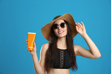 Young woman with sun protection cream on blue background