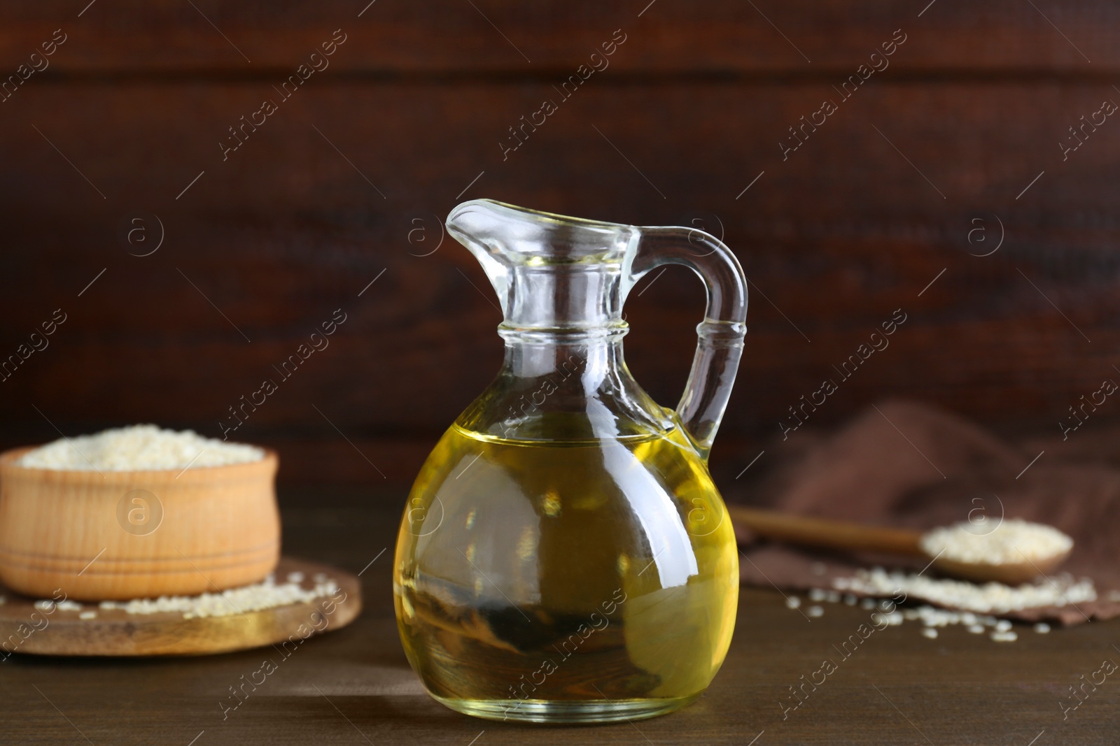Photo of Jug of organic sesame oil and seeds on wooden table