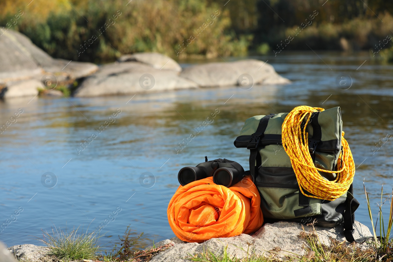 Photo of Set of camping equipment with sleeping bag on rock outdoors. Space for text