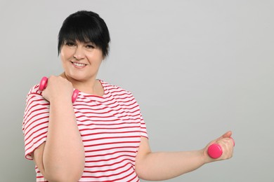 Photo of Happy overweight mature woman doing exercise with dumbbells on grey background, space for text