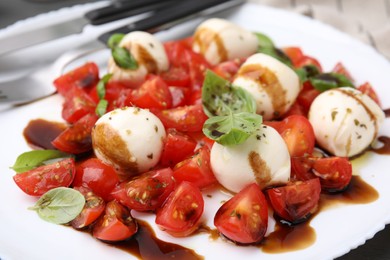 Photo of Tasty salad Caprese with tomatoes, mozzarella balls, basil and balsamic vinegar on plate, closeup