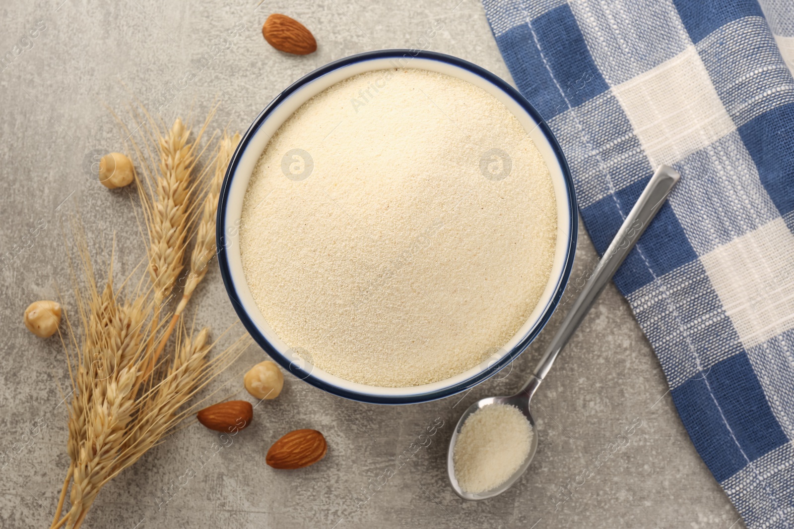 Photo of Uncooked organic semolina, spikelets and different nuts on grey table, flat lay