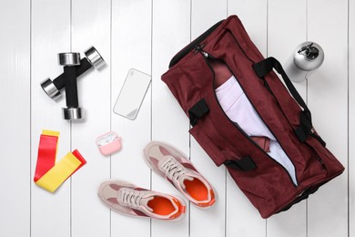 Photo of Gym bag and sports equipment on white wooden background, flat lay