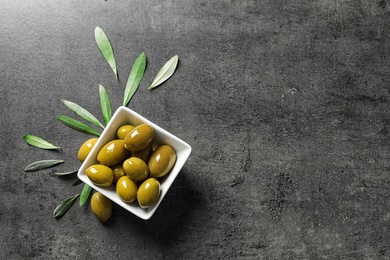 Ripe olives covered with oil in dish and leaves on table, top view