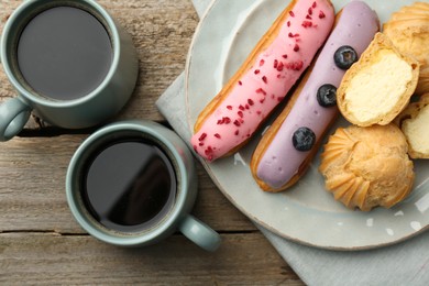 Photo of Aromatic coffee in cups, tasty eclairs and profiteroles on wooden table, top view