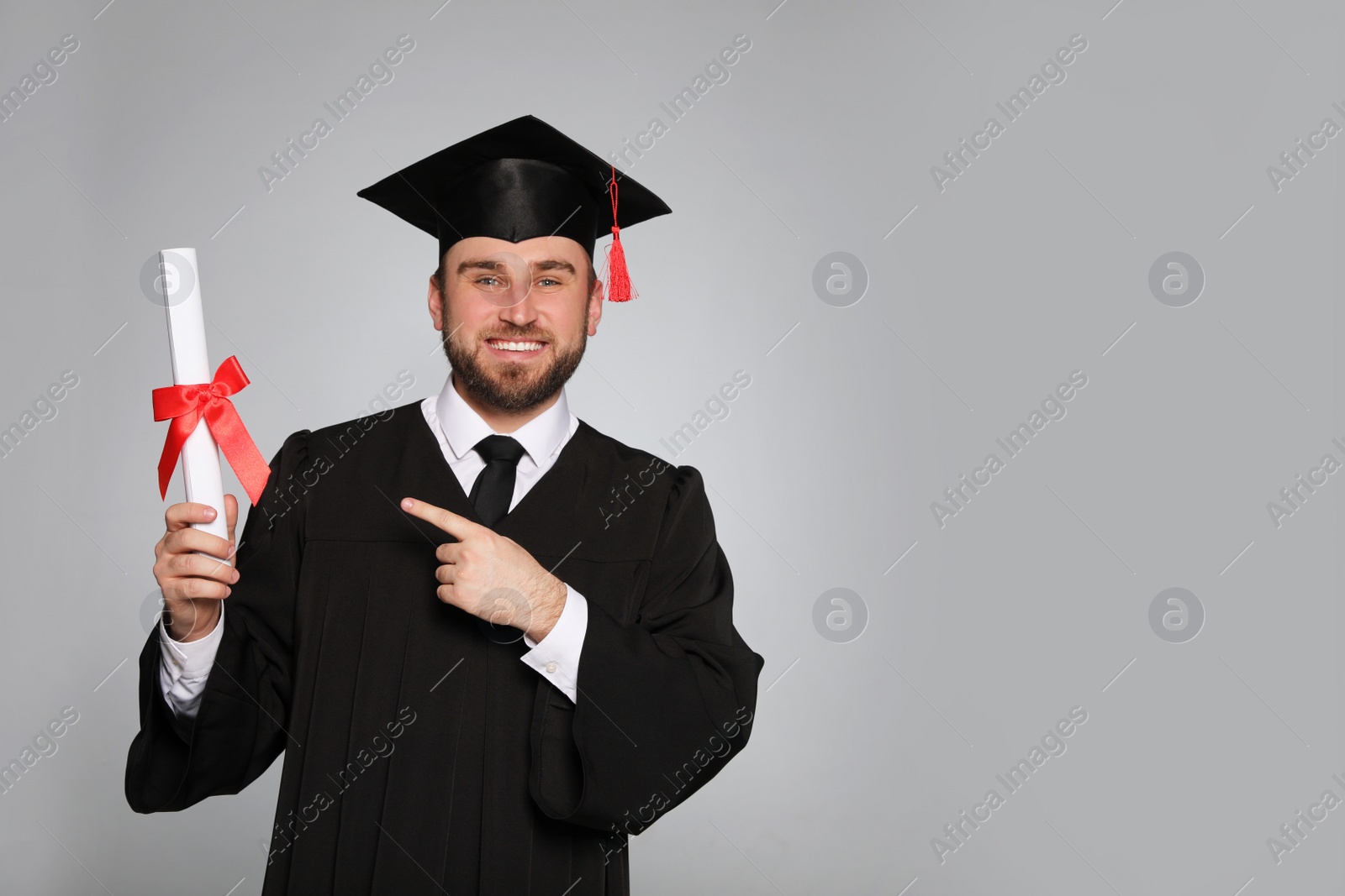 Photo of Happy student with graduation hat and diploma on grey background. Space for text