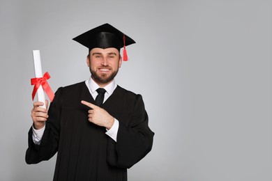 Happy student with graduation hat and diploma on grey background. Space for text