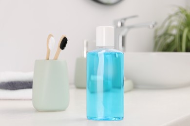 Bottle of mouthwash and toothbrushes on white table in bathroom