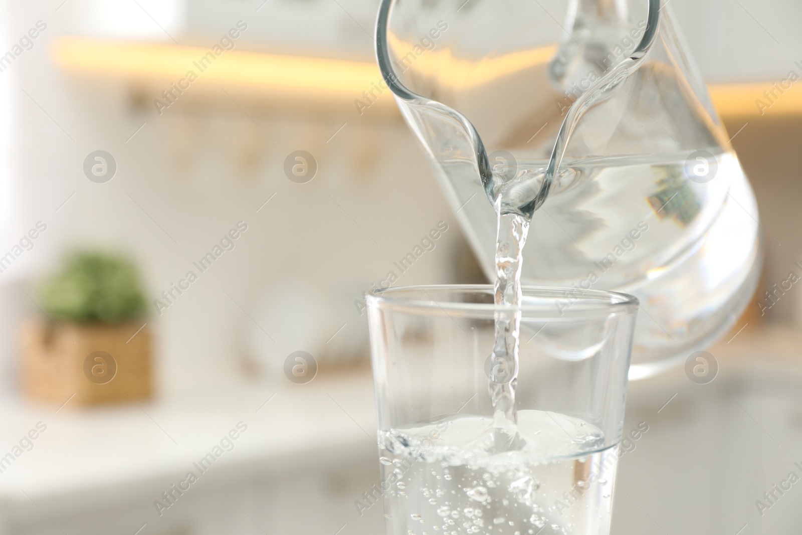 Photo of Pouring water from jug into glass in kitchen, closeup. Space for text