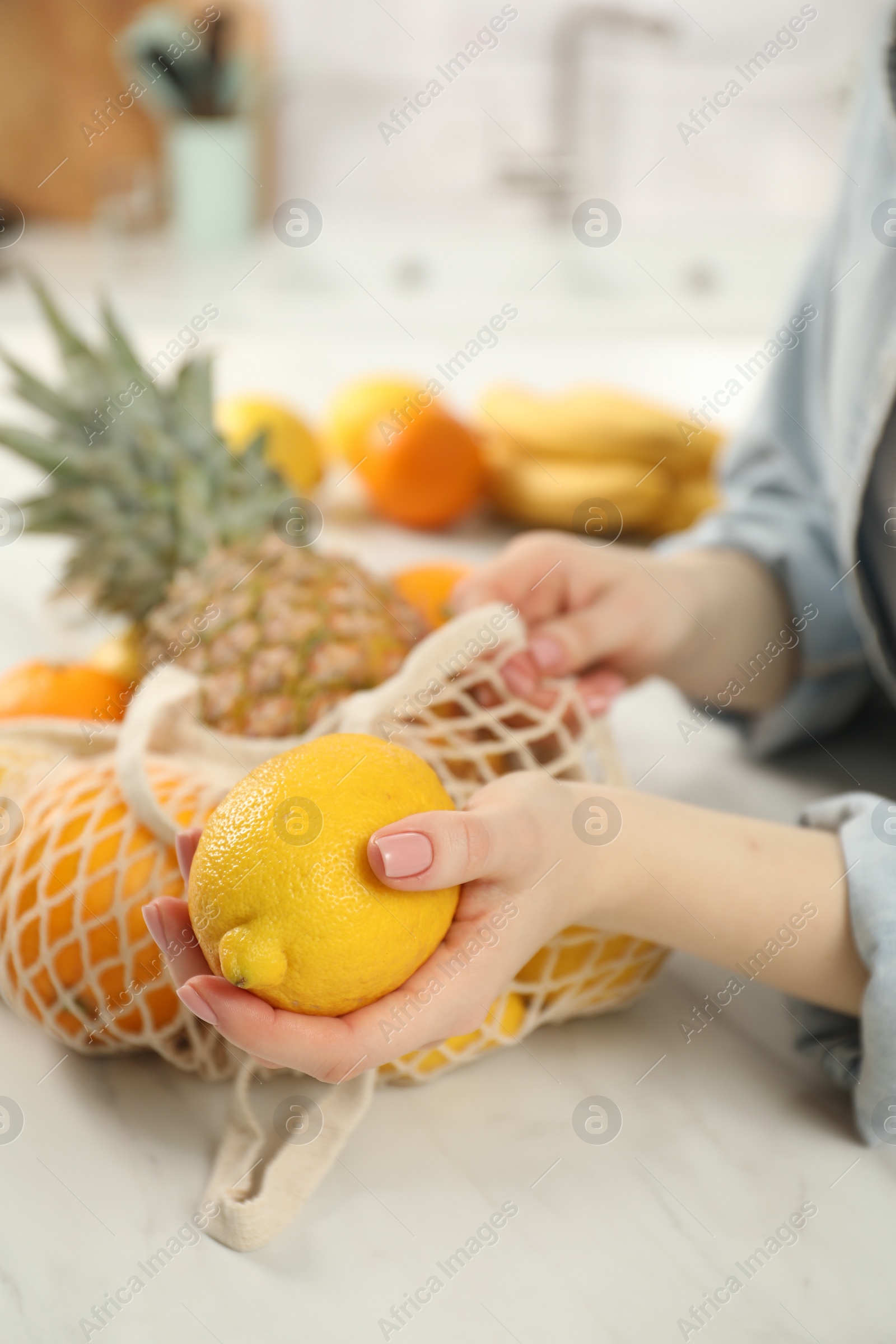 Photo of Woman with string bag of fresh fruits and lemon at light table, closeup