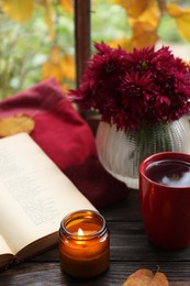 Photo of Burning scented candle, cup of tea and book on wooden table. Autumn still life