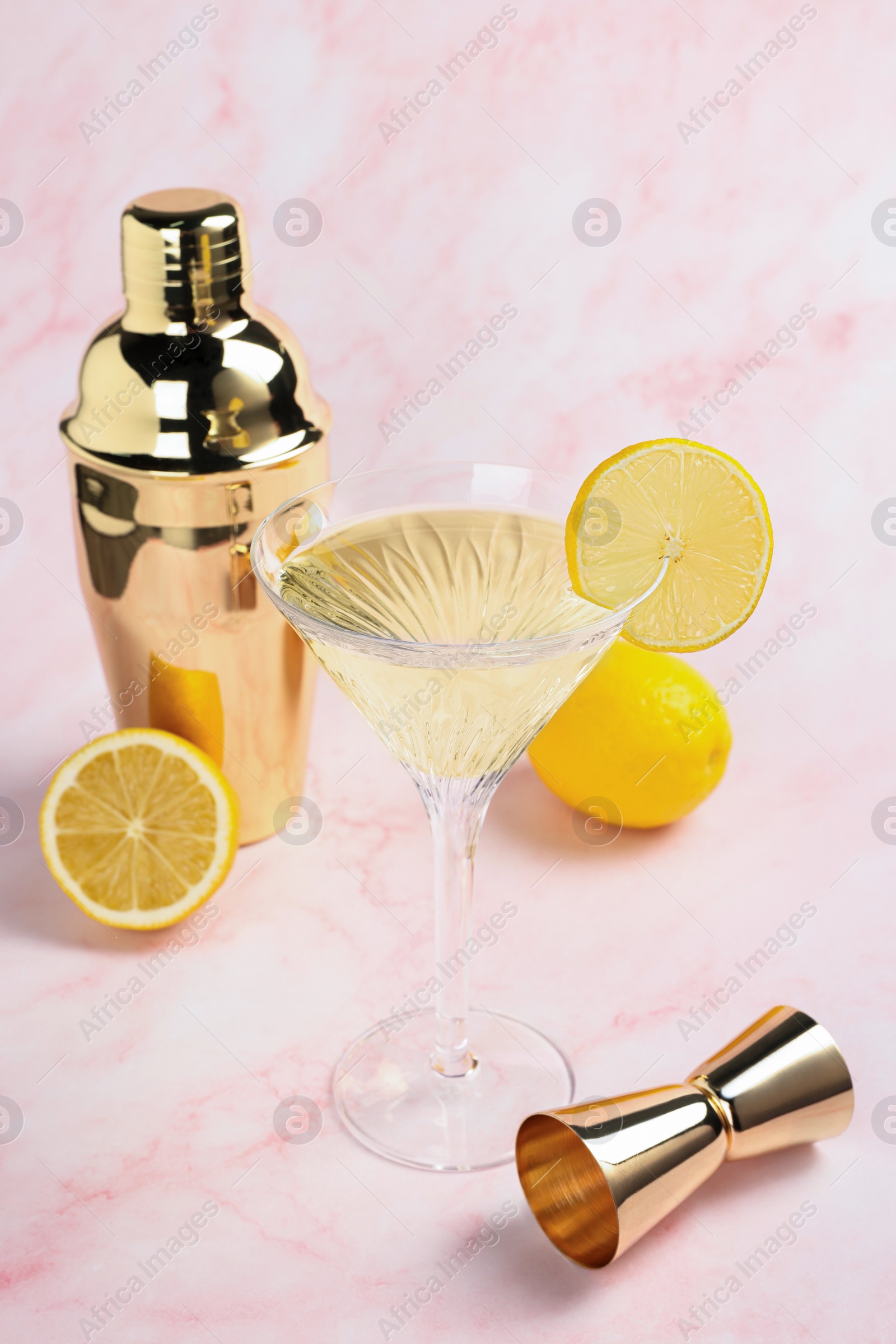 Photo of Martini glass of refreshing cocktail with lemon slice and fresh fruits near shaker on pink marble background