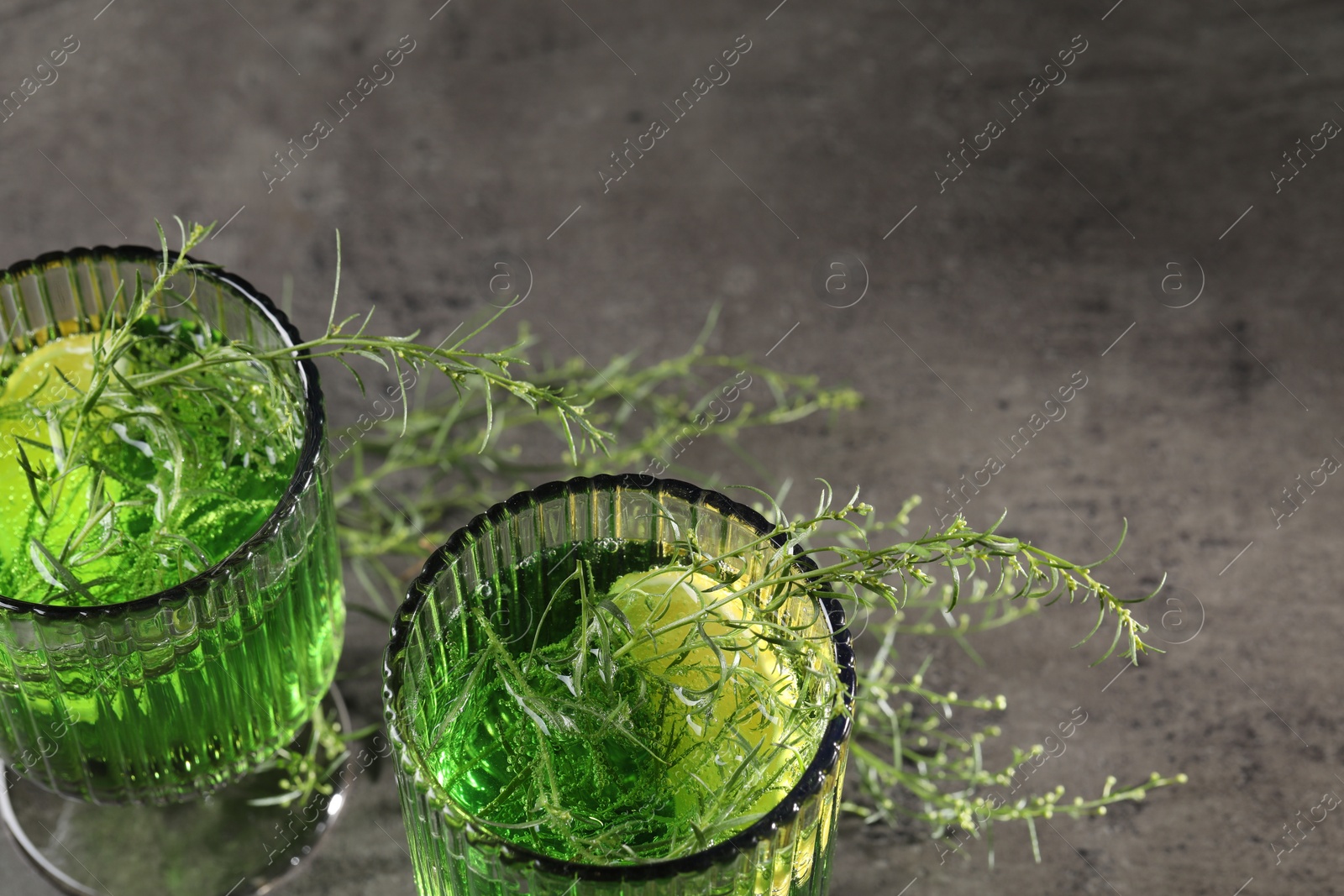 Photo of Glasses of homemade refreshing tarragon drink and sprigs on grey table, above view with space for text