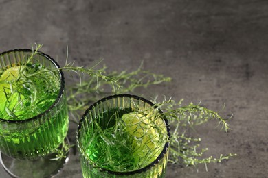 Glasses of homemade refreshing tarragon drink and sprigs on grey table, above view with space for text