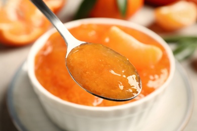 Photo of Spoon with delicious tangerine over bowl, closeup