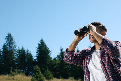 Photo of Man looking through binoculars outdoors on sunny day