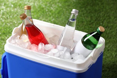 Photo of Blue plastic cool box with drinks and ice cubes on green grass
