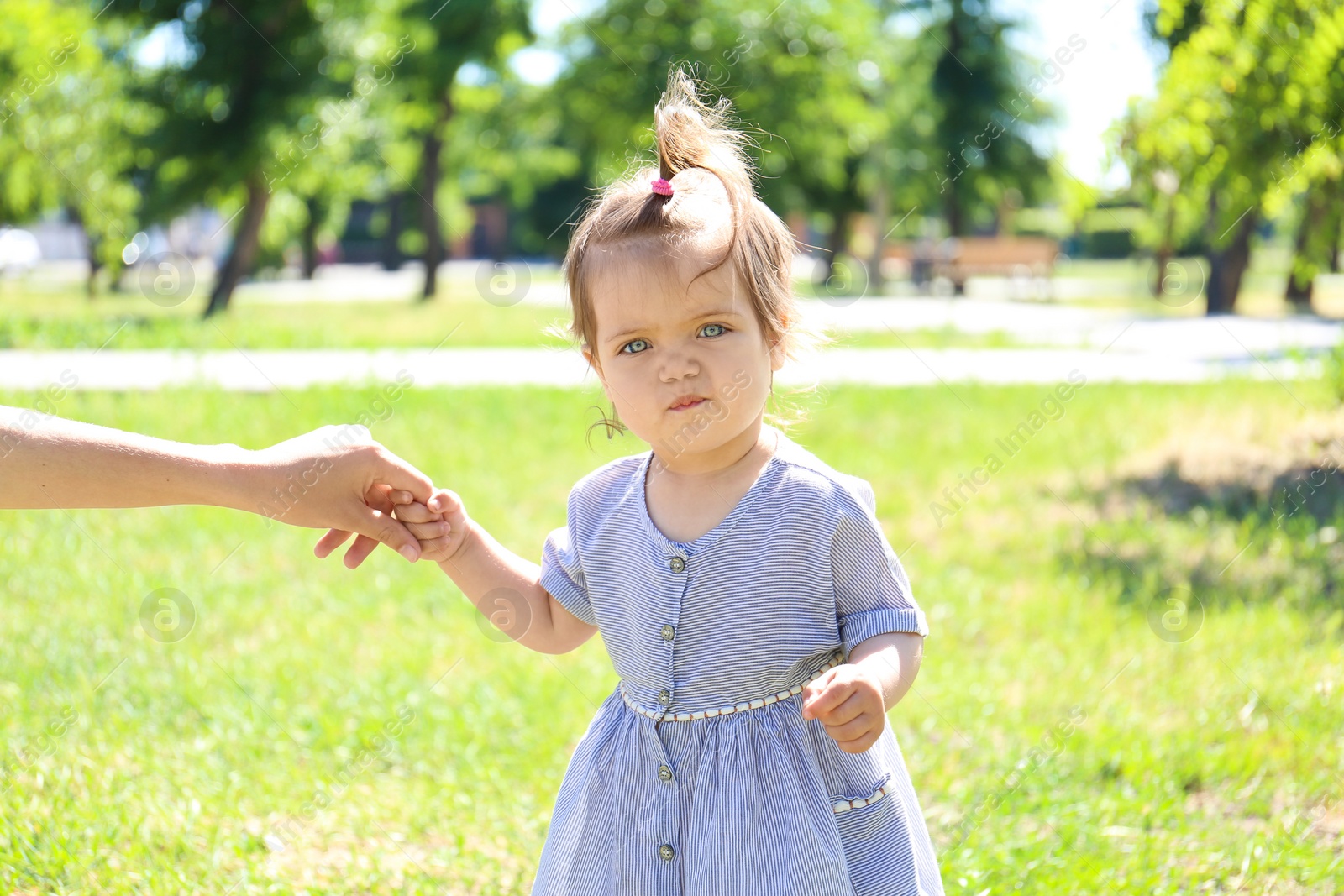 Photo of Adorable baby girl holding mother's hand while learning to walk outdoors