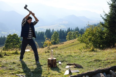 Photo of Handsome man with axe cutting firewood on hill