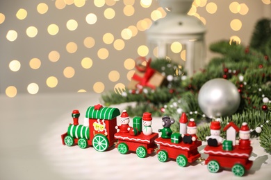 Photo of Toy train and Christmas decor on white table against blurred lights