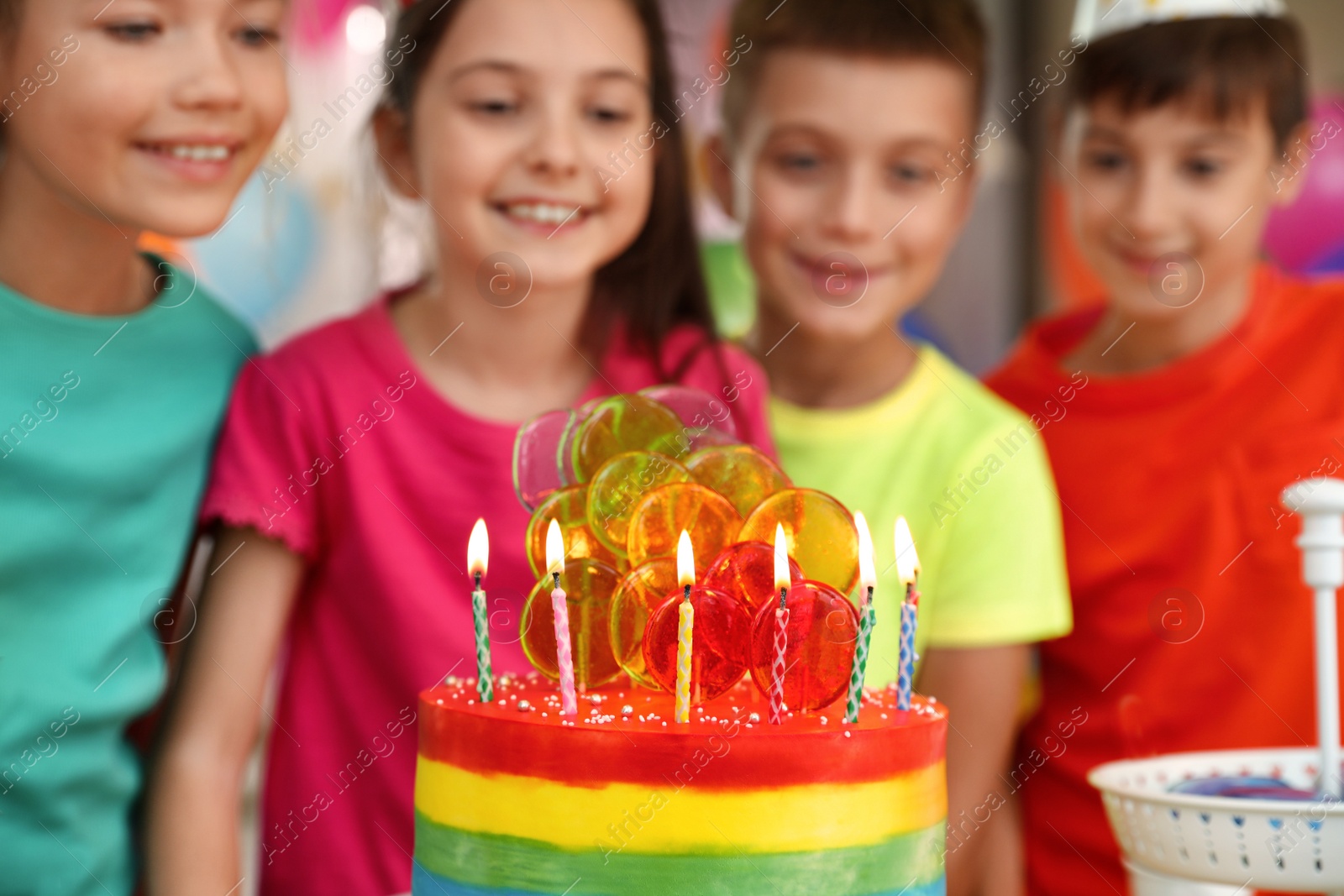 Photo of Children near cake with candles at birthday party indoors, closeup