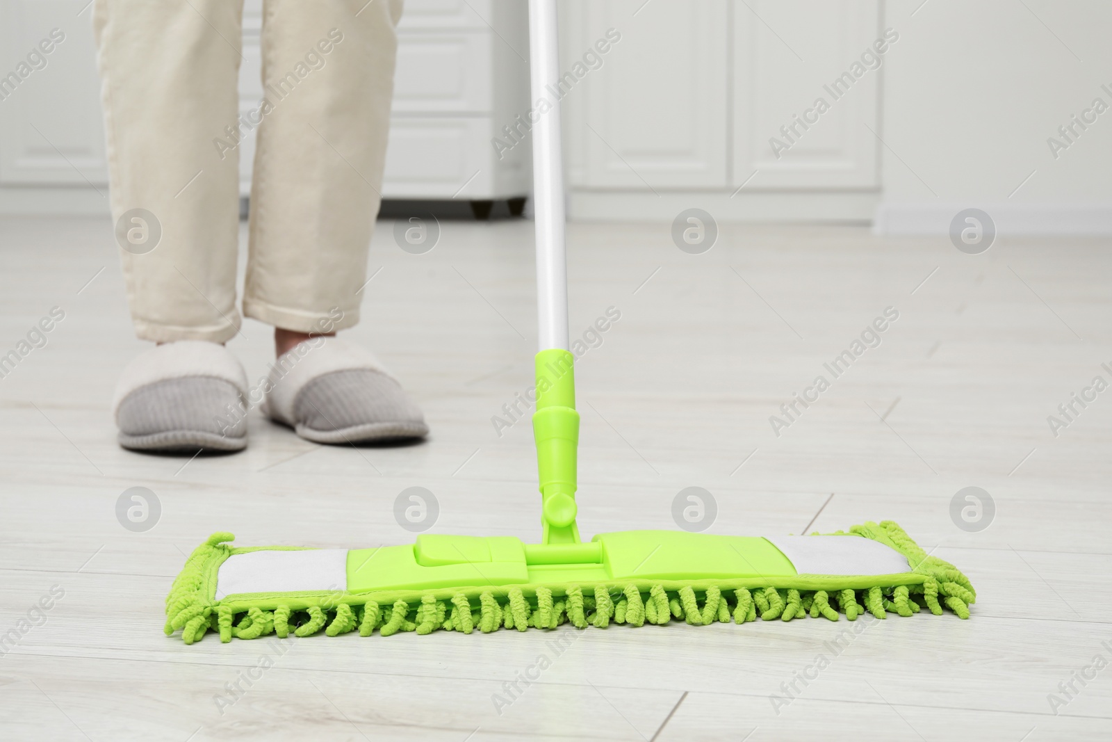 Photo of Woman cleaning dirty white parquet floor with mop indoors, closeup
