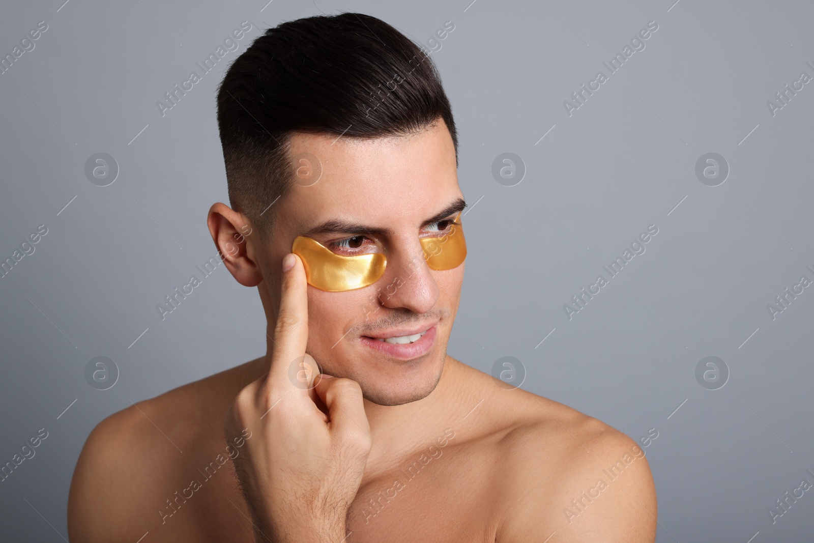 Photo of Man applying golden under eye patch on grey background