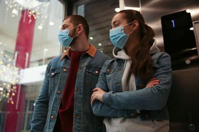 Photo of Couple wearing disposable masks in elevator. Dangerous virus
