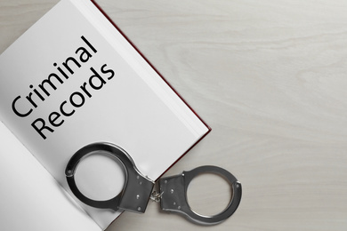 Image of Book with words CRIMINAL RECORDS and handcuffs on white wooden background, top view. Space for text
