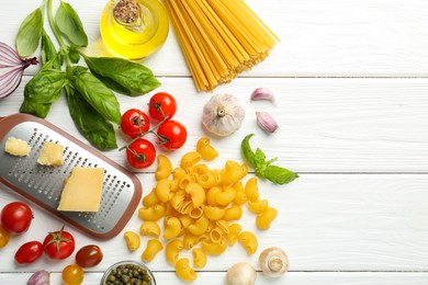 Different types of pasta, grater and products on white wooden table, flat lay. Space for text