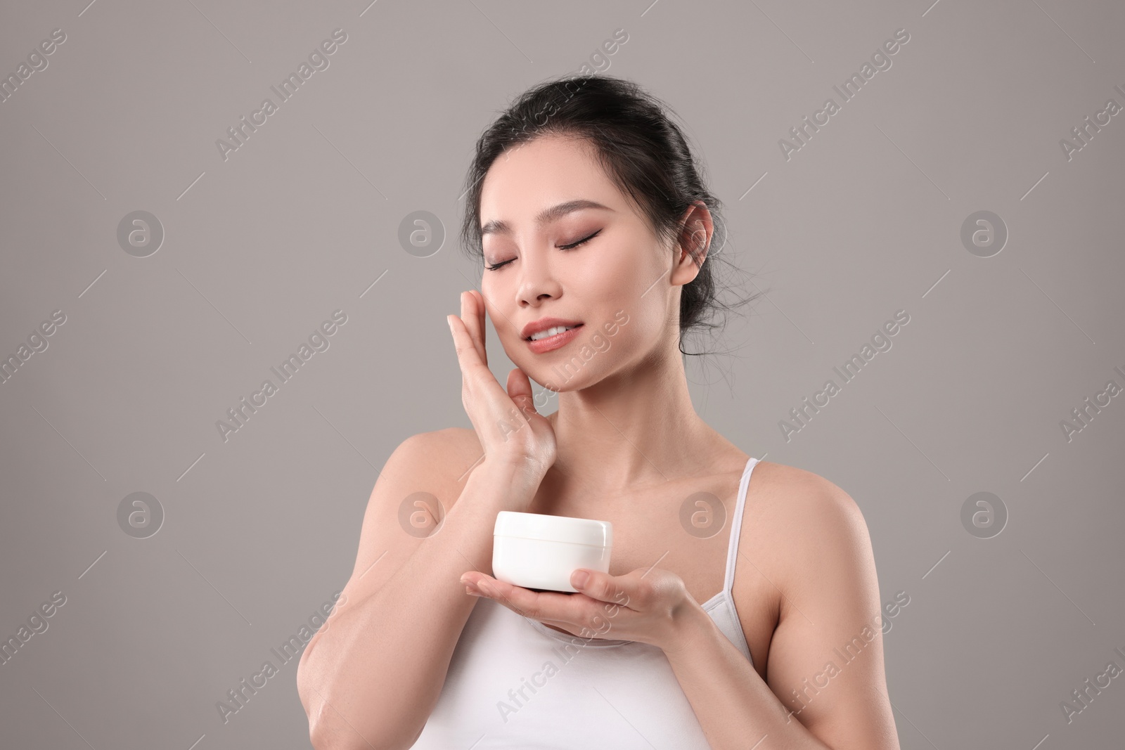 Photo of Happy woman applying face cream on grey background