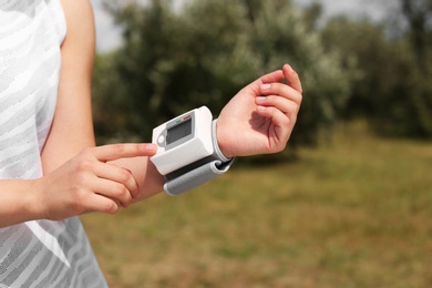 Photo of Young woman checking pulse with medical device after training in park, closeup
