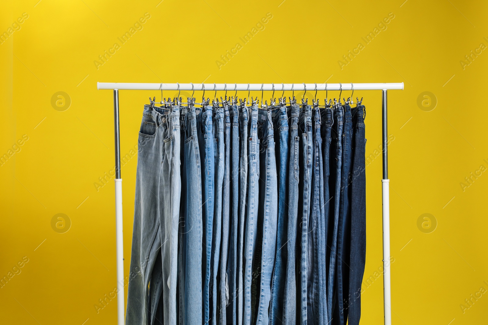 Photo of Rack with different jeans on yellow background