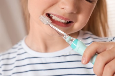 Photo of Little girl brushing her teeth with electric toothbrush on blurred background, closeup