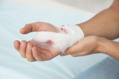 Photo of Young man with bandage on injured hand in clinic, closeup. First aid