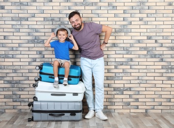Photo of Man and his son with suitcases near brick wall. Vacation travel