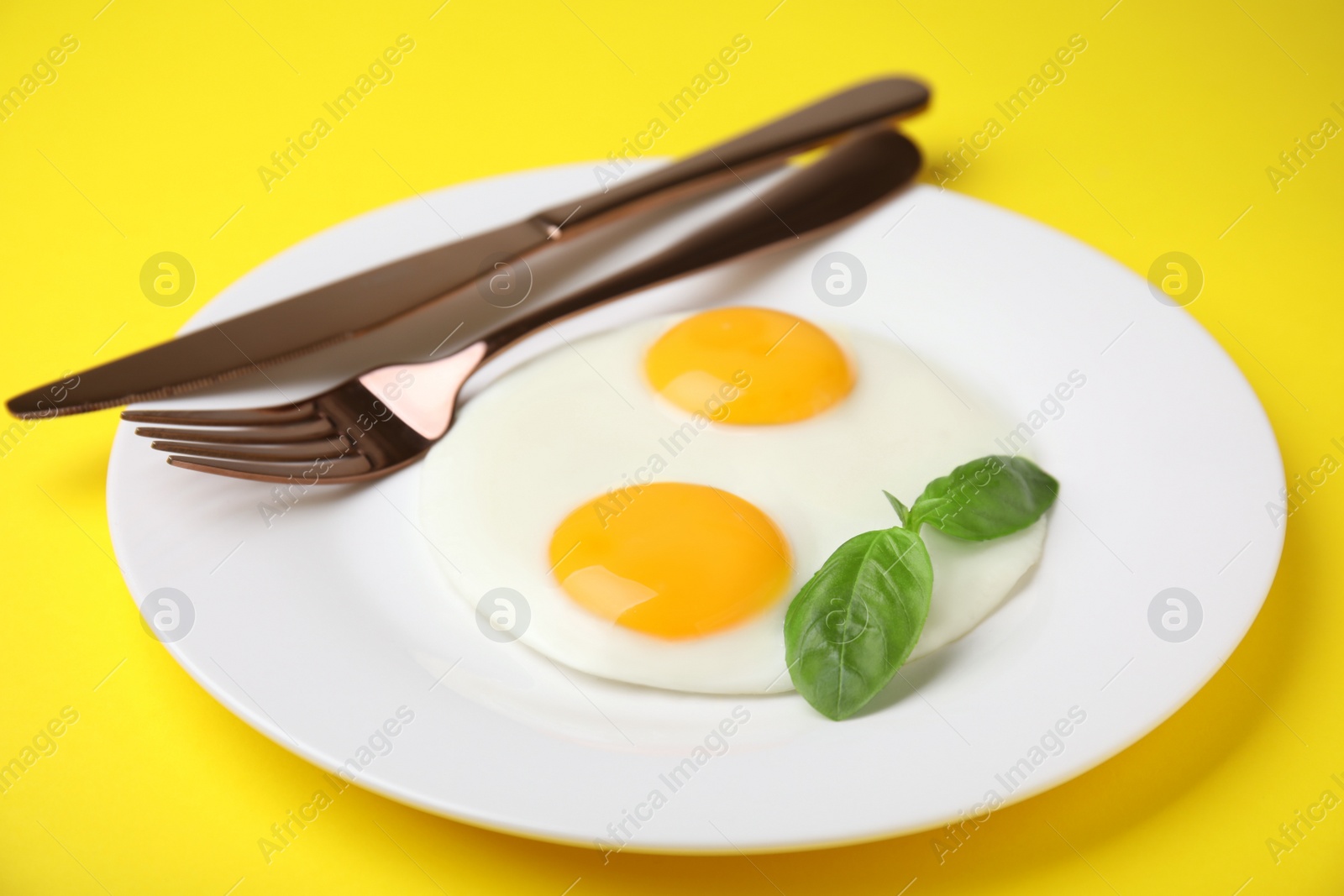 Photo of Tasty fried eggs with basil in plate on yellow background, closeup