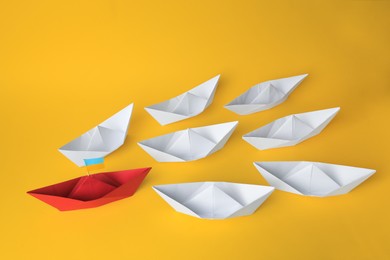 Photo of Group of paper boats following red one on yellow background. Leadership concept