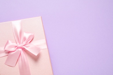 Photo of Pink gift box on violet background, top view. Space for text
