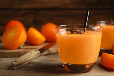 Tasty persimmon smoothie with anise and straw on wooden table, closeup. Space for text