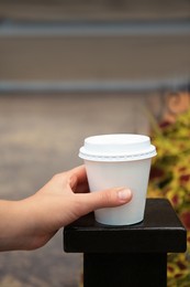 Woman with cardboard cup of coffee near flower bed outdoors, closeup