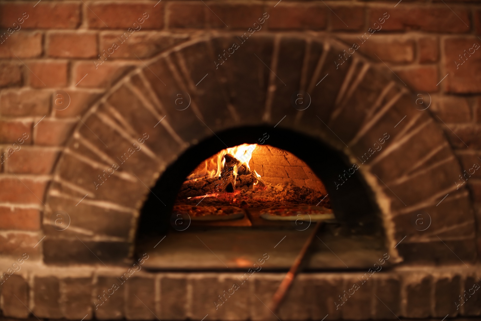 Photo of Brick oven with burning firewood and pizzas indoors