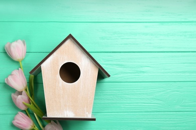 Photo of Beautiful bird house and pink tulips on turquoise wooden background, flat lay. Spring composition with space for text