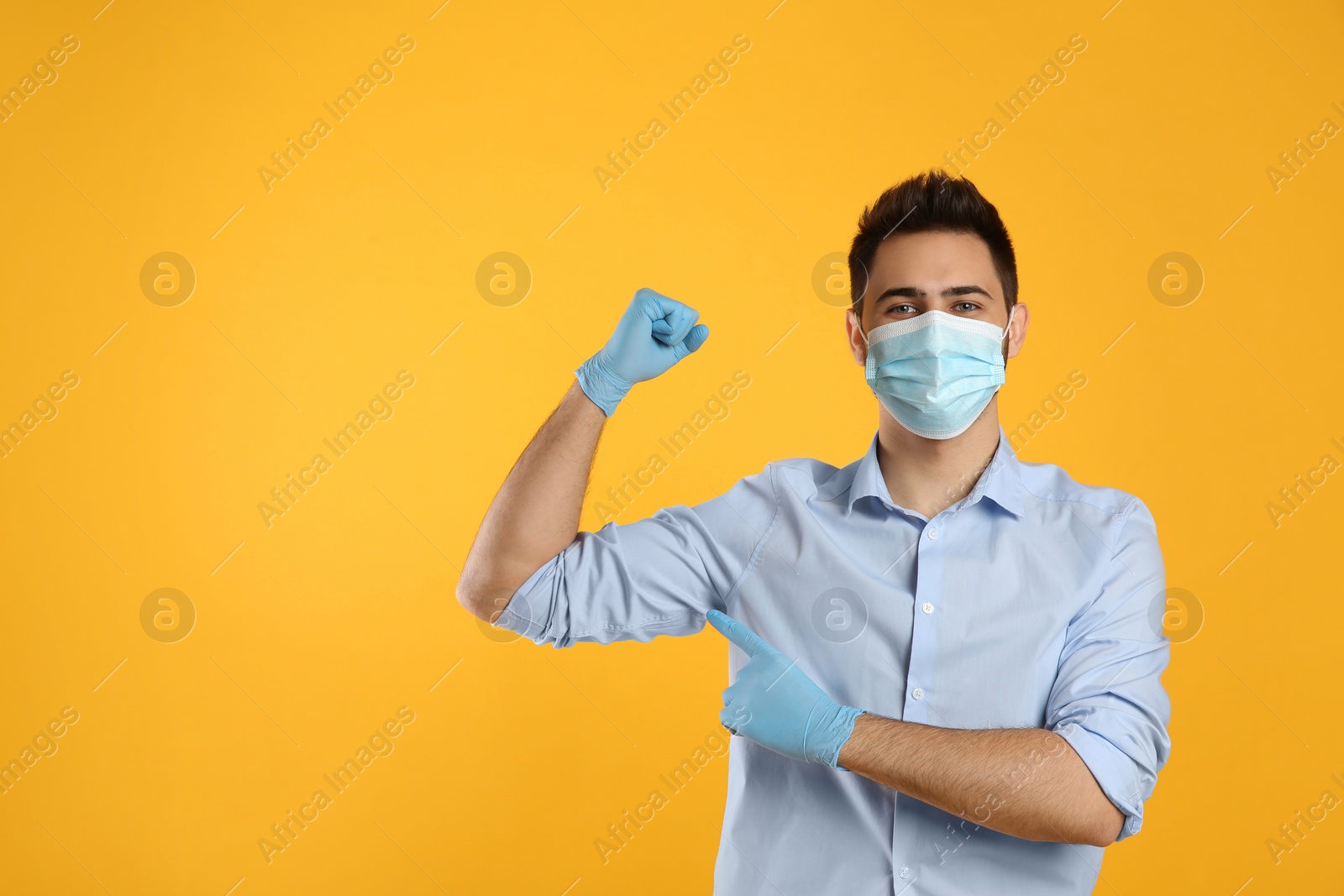 Photo of Man with protective mask and gloves showing muscles on yellow background, space for text. Strong immunity concept