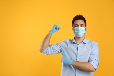 Man with protective mask and gloves showing muscles on yellow background, space for text. Strong immunity concept