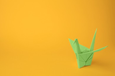 Photo of Origami art. Beautiful light green paper crane on orange background, space for text
