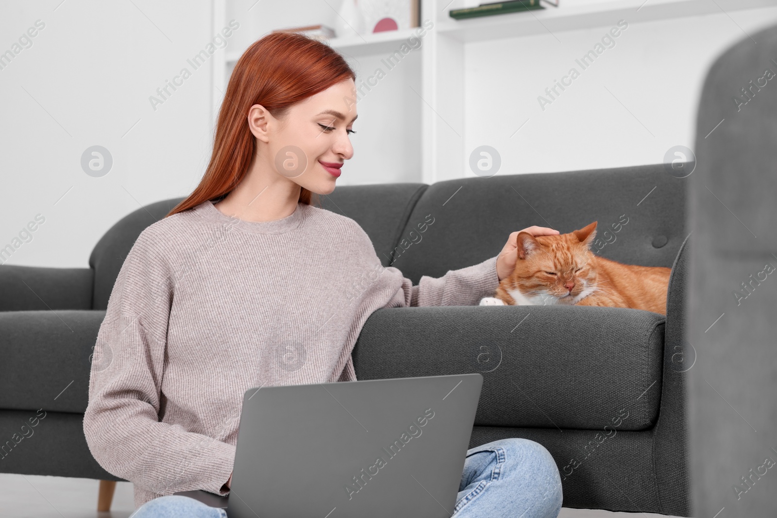 Photo of Woman stroking cat while working with laptop at home